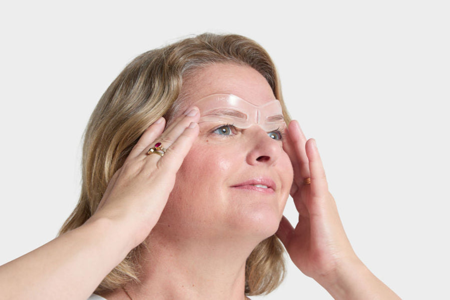 Woman applying the bold brow blueprint stencil on her face against a white background